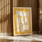 Framed artwork with 'WONDERFUL' text on a yellow background, leaning against a wooden wall.