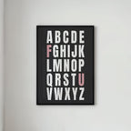 Framed alphabet poster with the letters F and U highlighted in pink on a light gray wall.