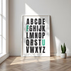 Framed alphabet poster with the letters F and U highlighted in teal on a wall with a plant on a wooden floor.