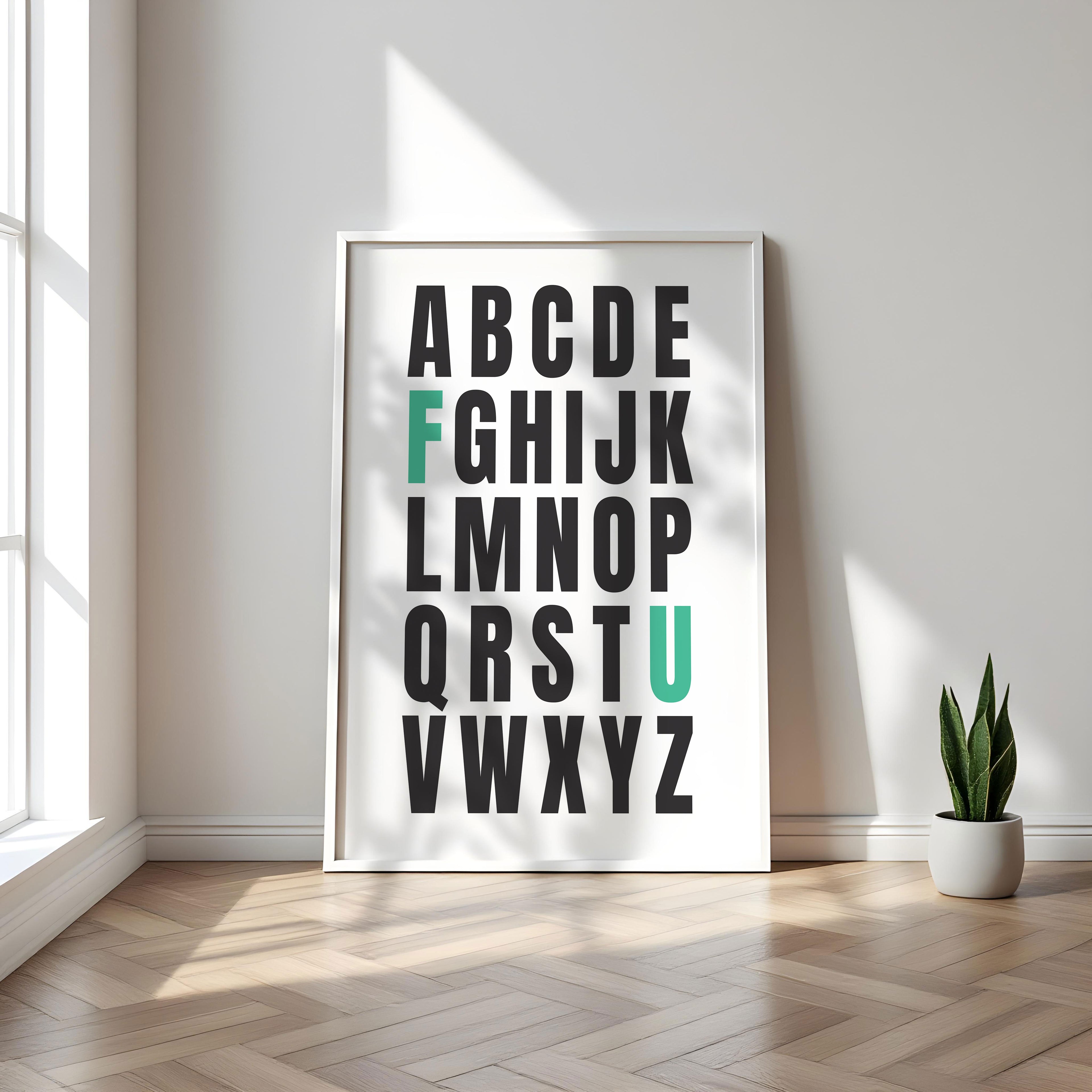 Framed alphabet poster with the letters F and U highlighted in teal on a wall with a plant on a wooden floor.