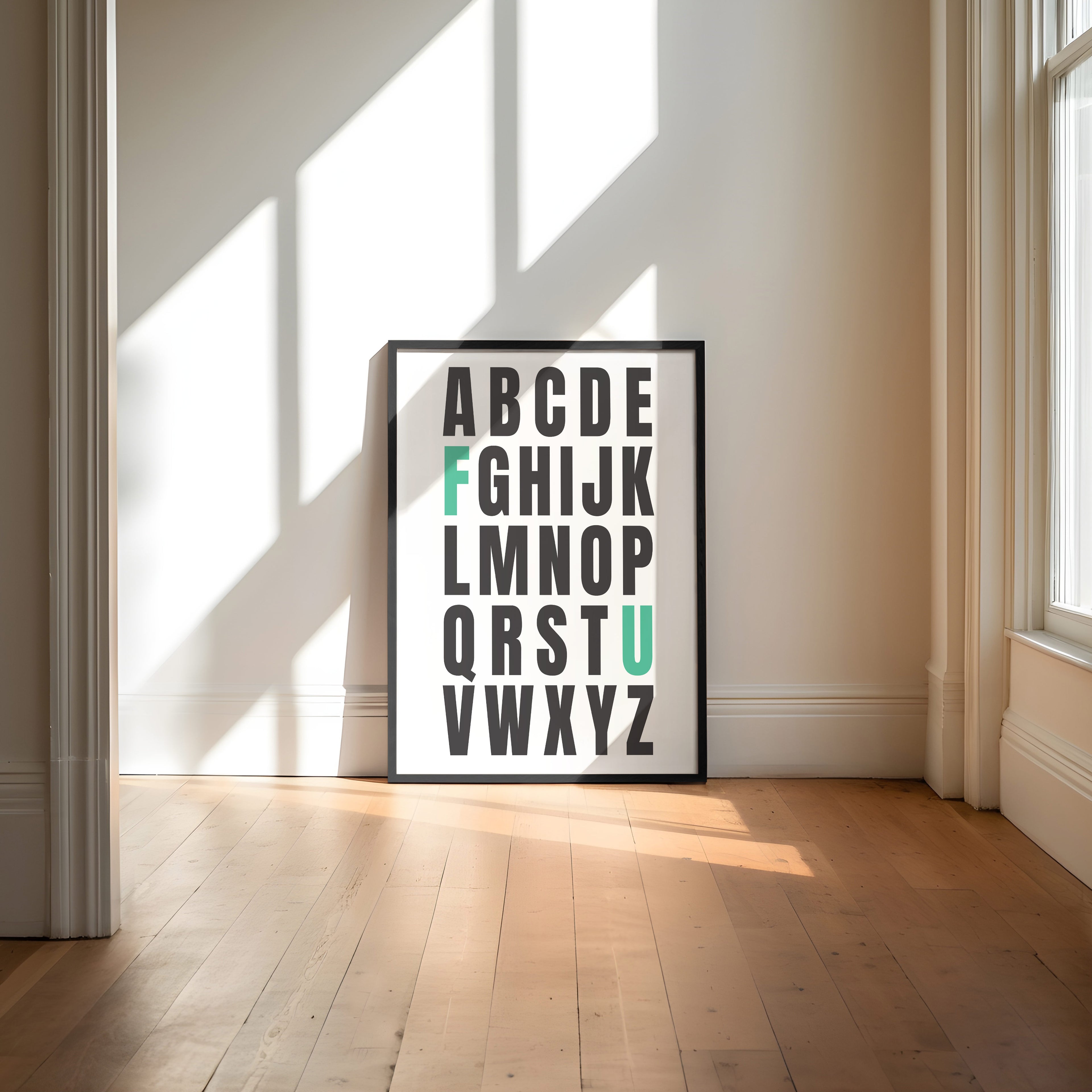 Framed alphabet poster with the letters F and U highlighted in teal on a wall with sunlight casting shadows.