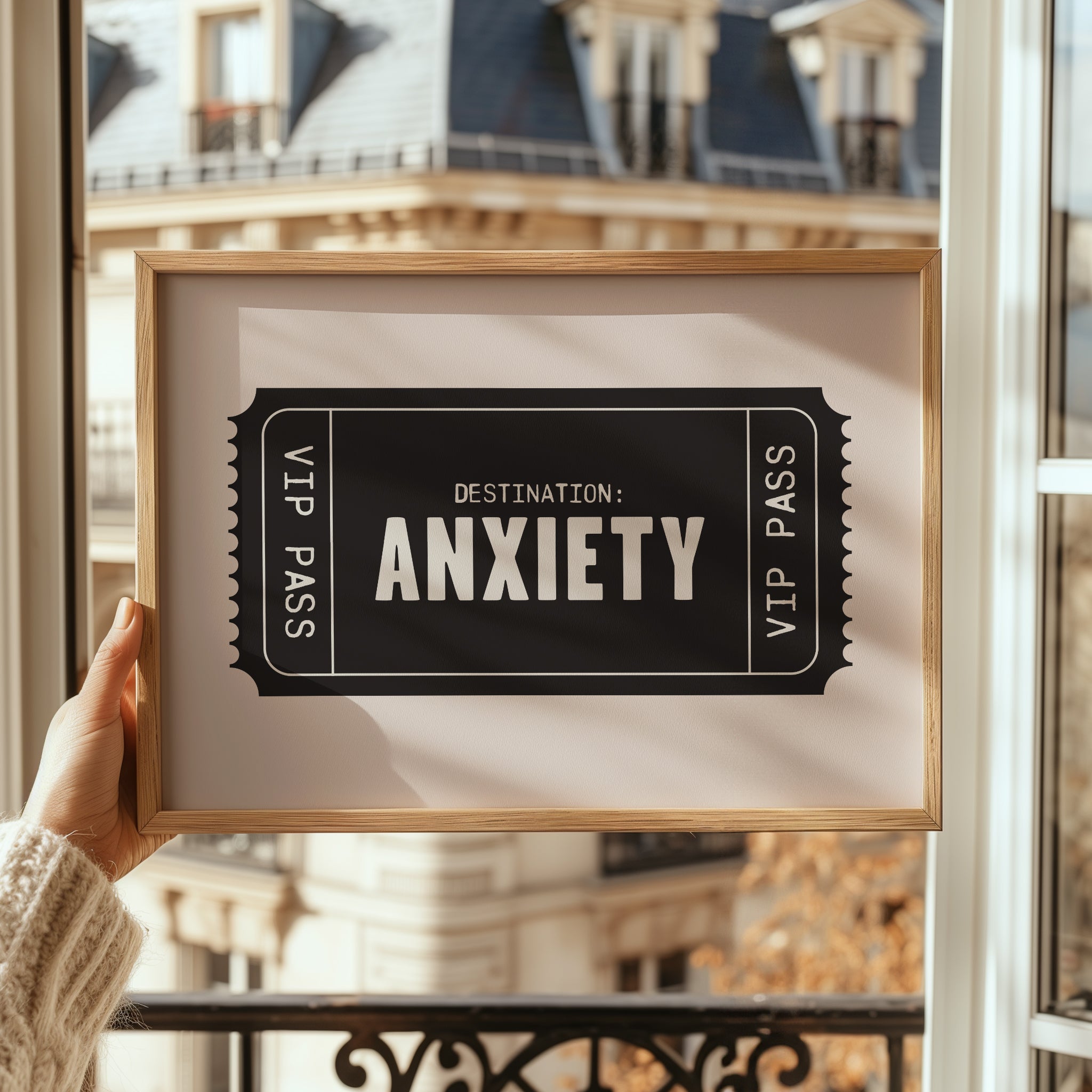 Framed picture of a ticket with 'Destination: Anxiety' text held against a blurred building background.