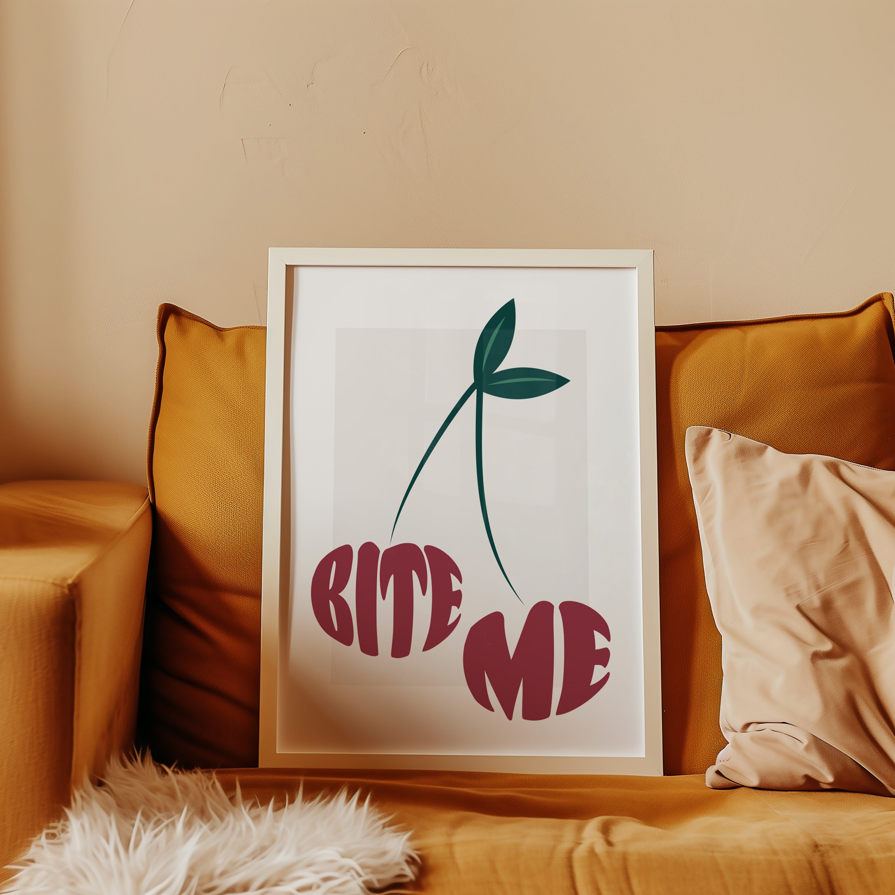 Framed artwork with 'BITE ME' text in the shape of two cherries on a couch with pillows.