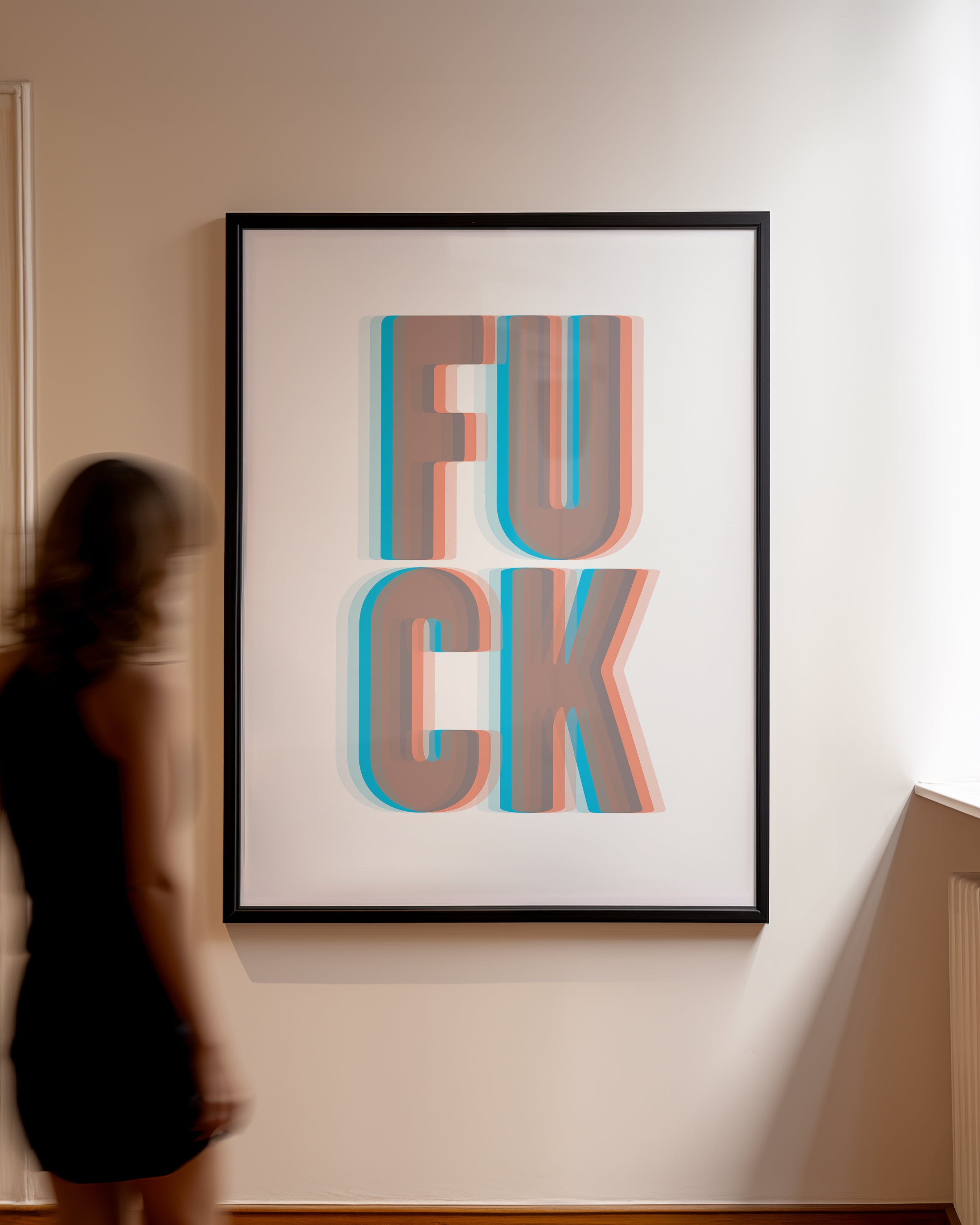 Framed artwork with the word 'Fuck' in a 3D effect on a wall, blurred figure in foreground