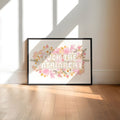 Framed artwork with floral design and text in a room with large windows.