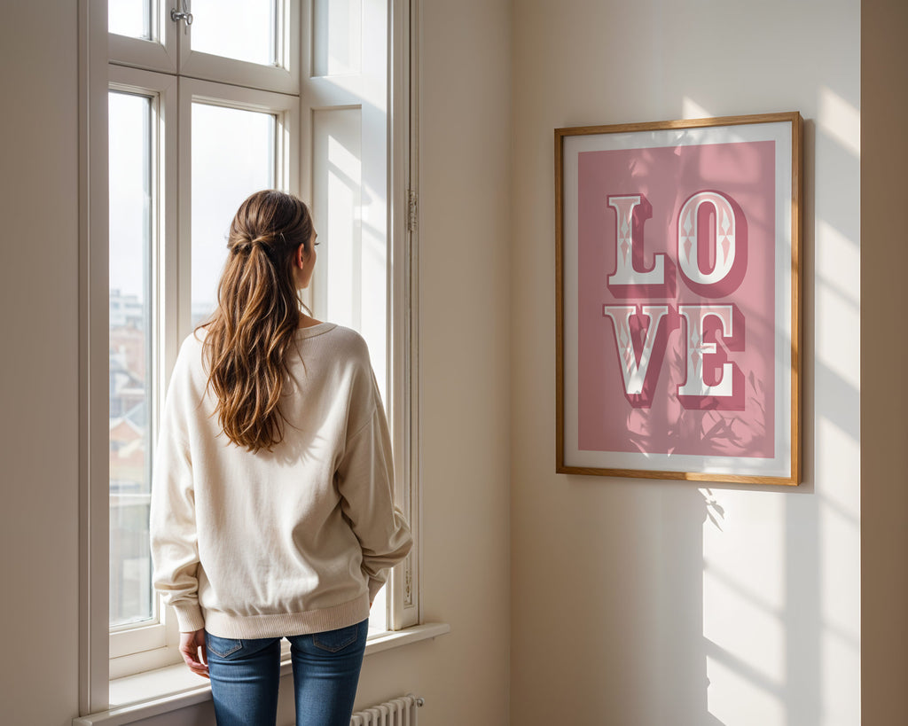 Woman standing by a window looking outside, with a 'LOVE' framed picture on the wall.