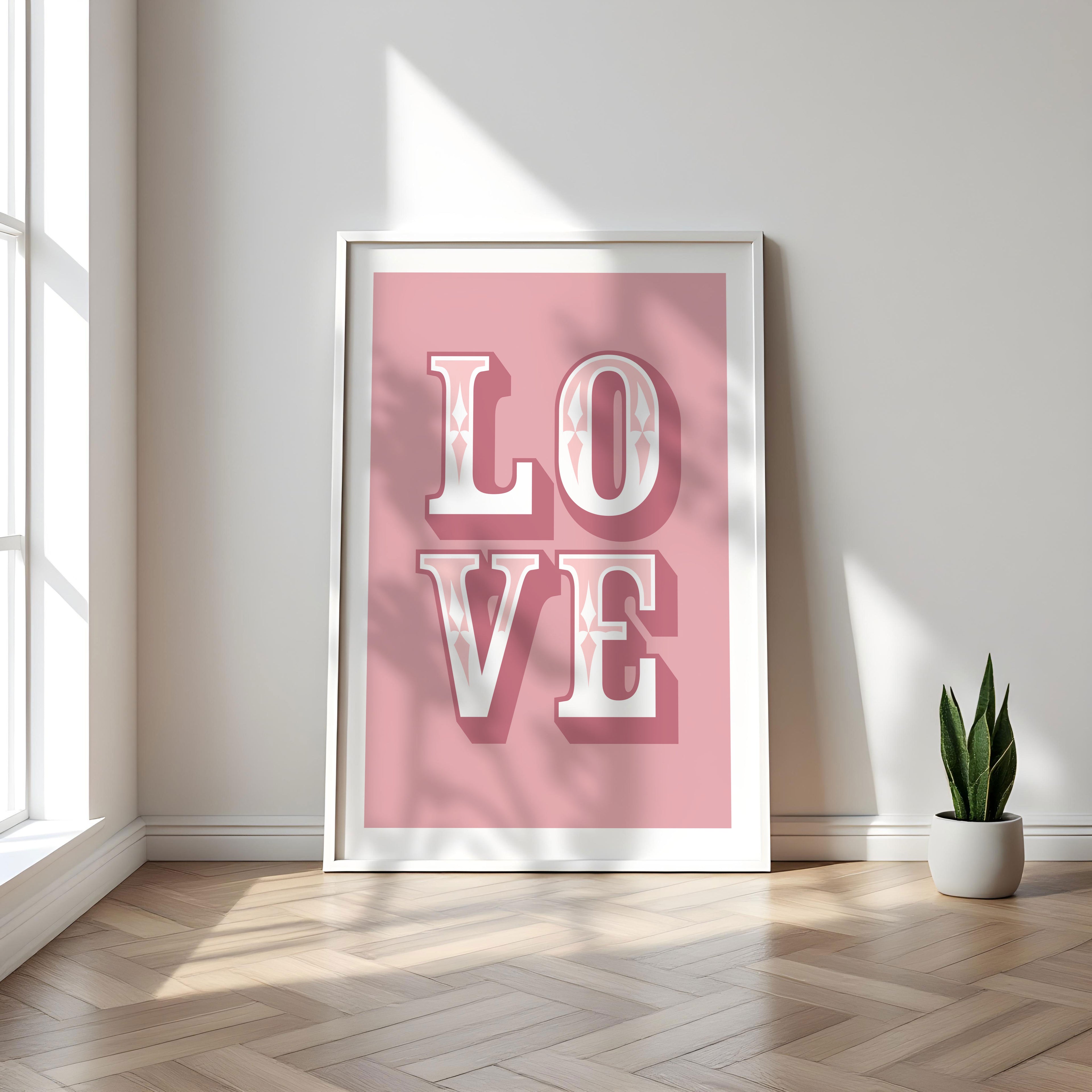 Framed poster with 'LOVE' on a pink background in a bright room with a plant.