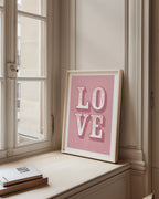 Framed 'LOVE' poster on a windowsill with books below