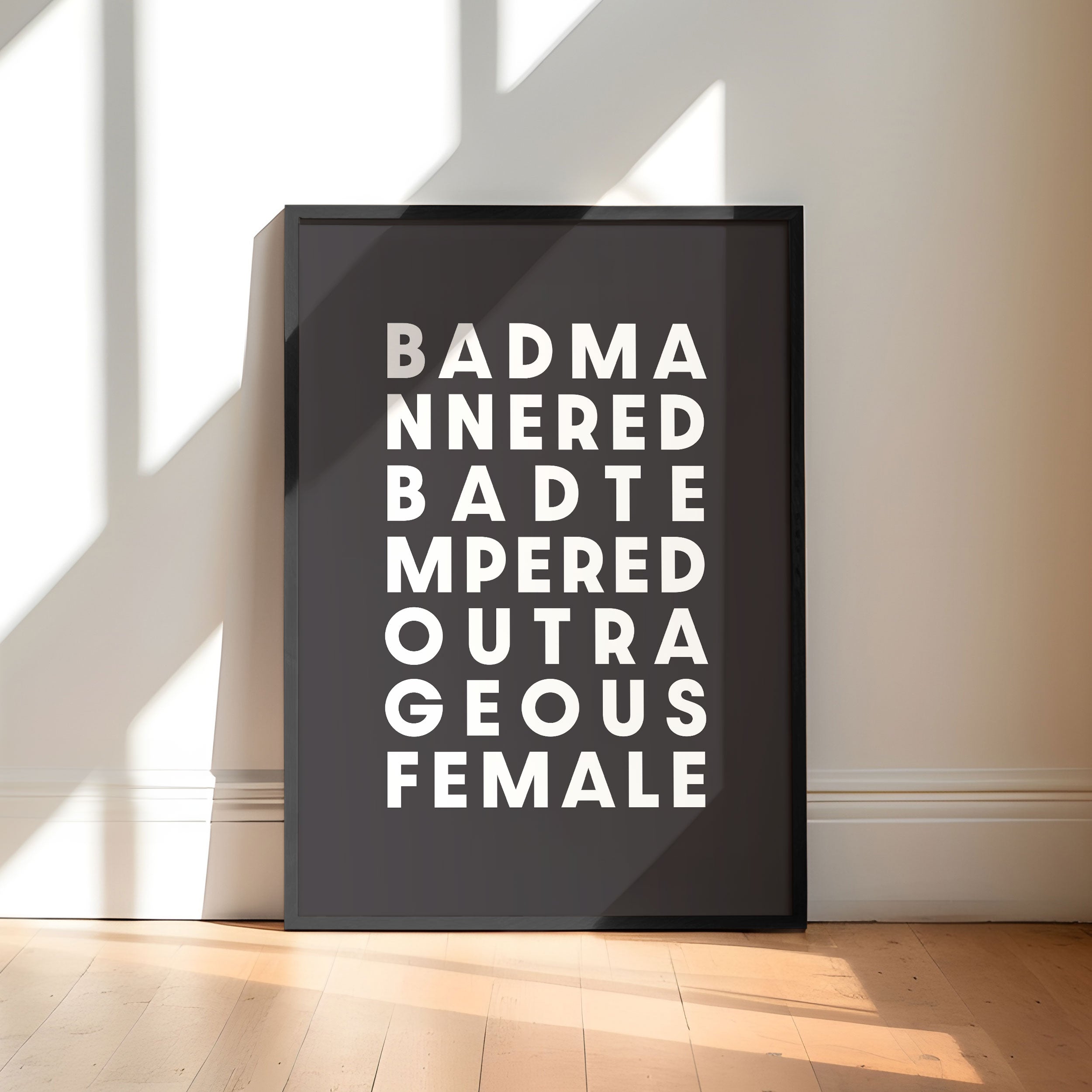 Framed poster with text saying 'Bad Mannered, Bad Tempered, Outrageous Female' on a white background.