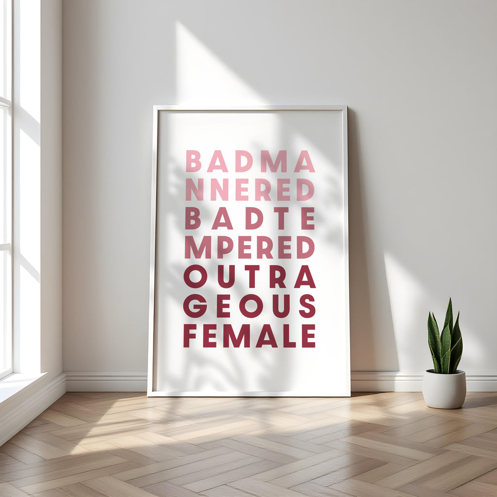 Framed poster with text saying 'Bad Mannered, Bad Tempered, Outrageous Female' in a minimalistic room with a plant.