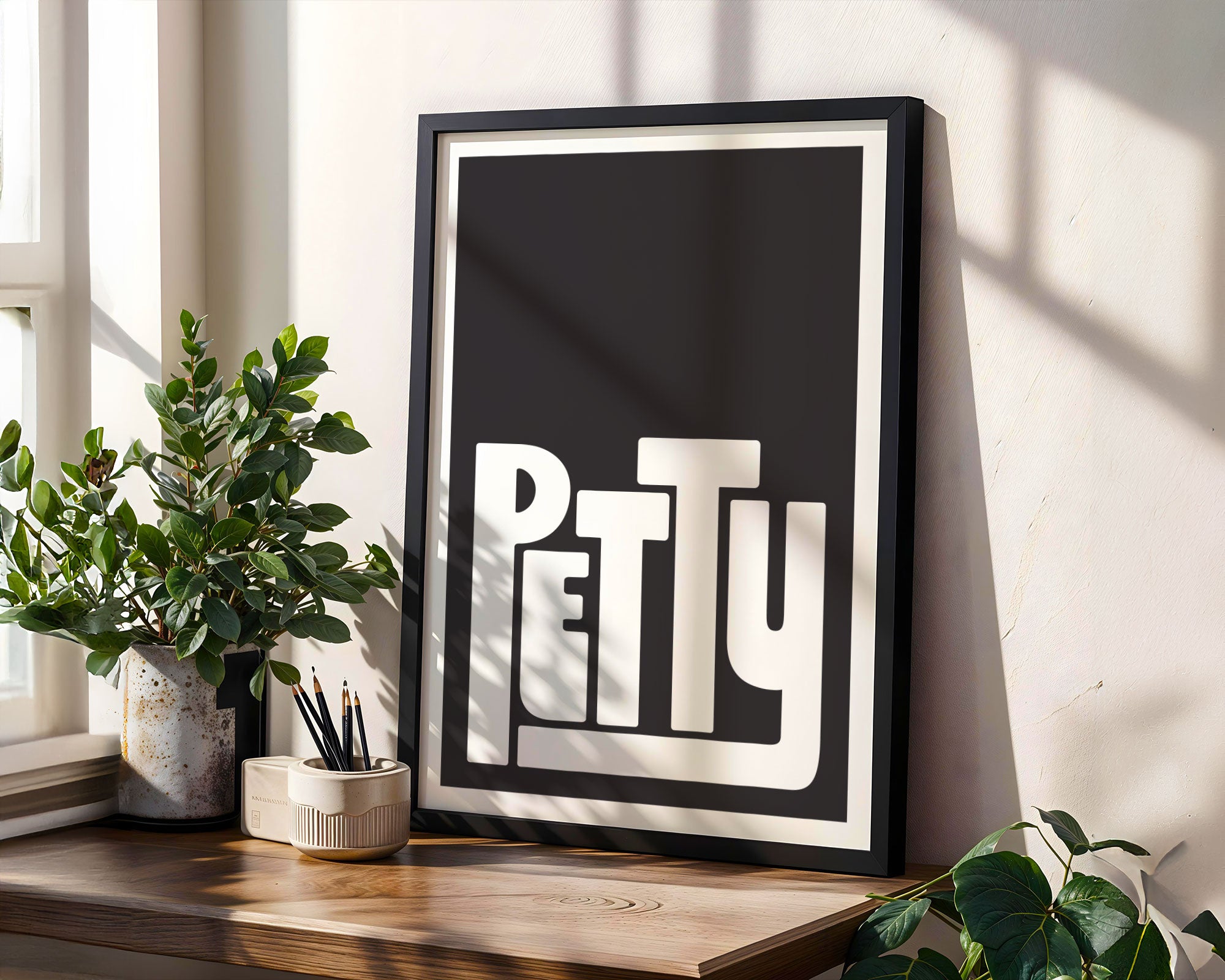 Framed artwork with the word 'PETTY' on a wooden shelf with plants