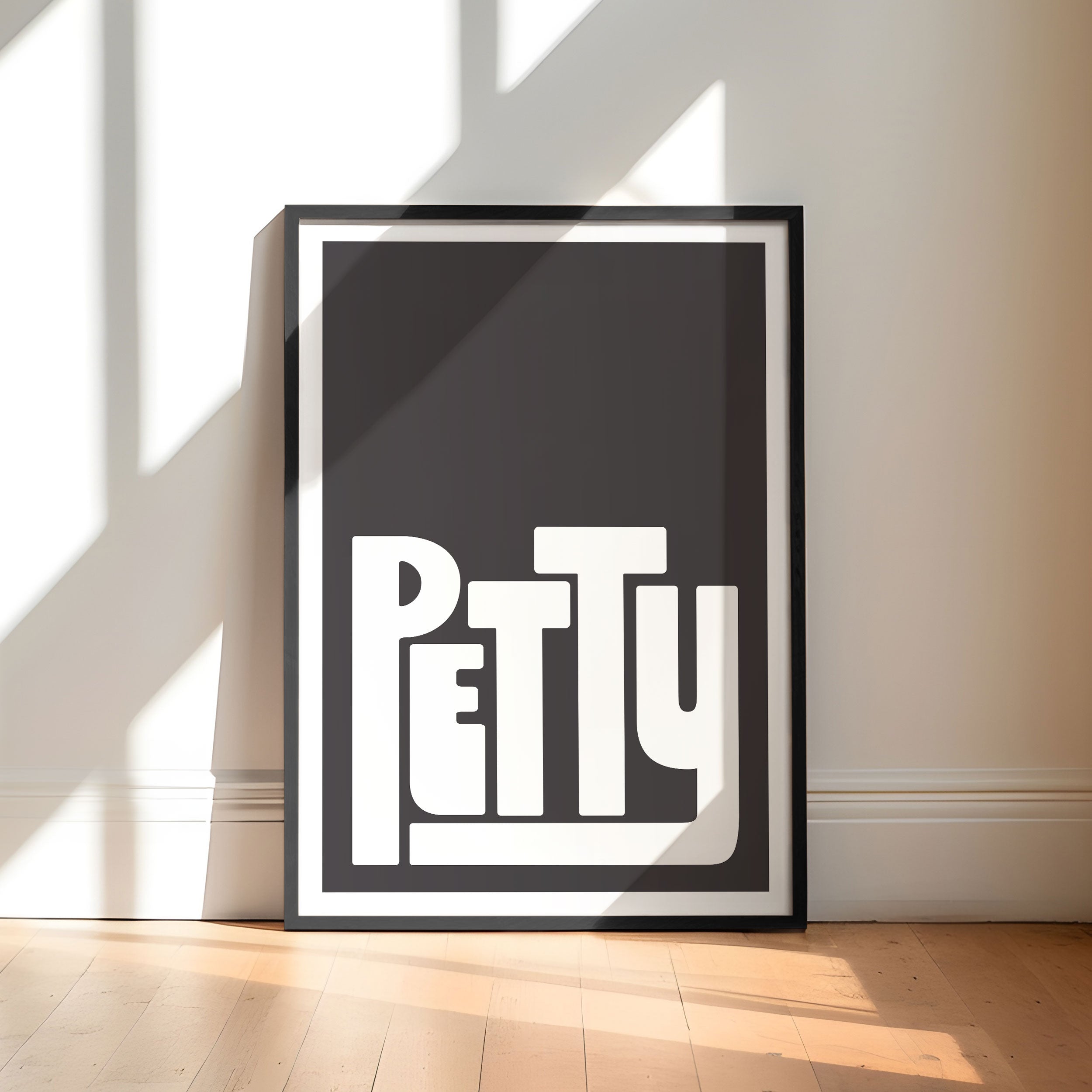 Framed artwork with the word 'Petty' on a black background in a minimalistic room.