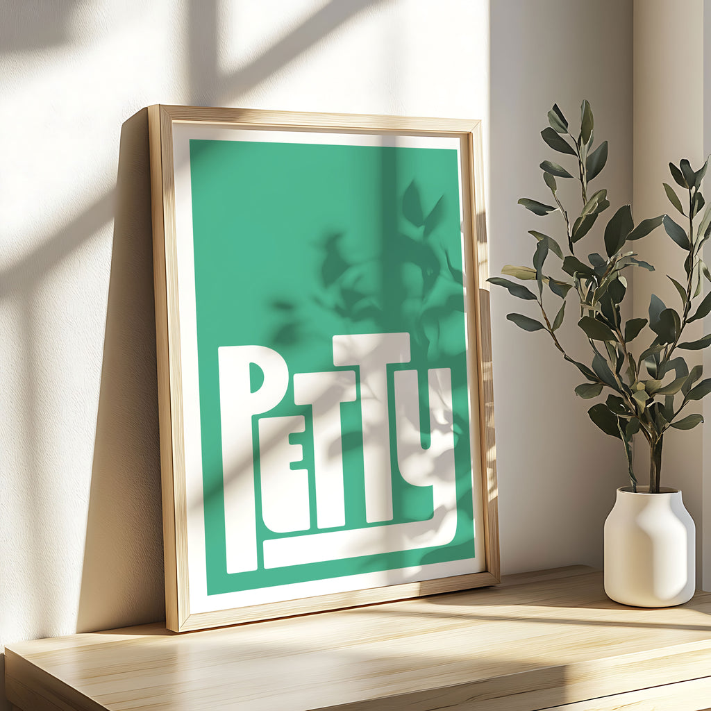 Framed artwork with 'Petty' on a shelf next to a plant