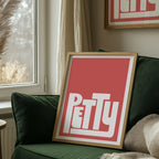 Framed artwork with the word 'PETTY' on a green couch next to a window.