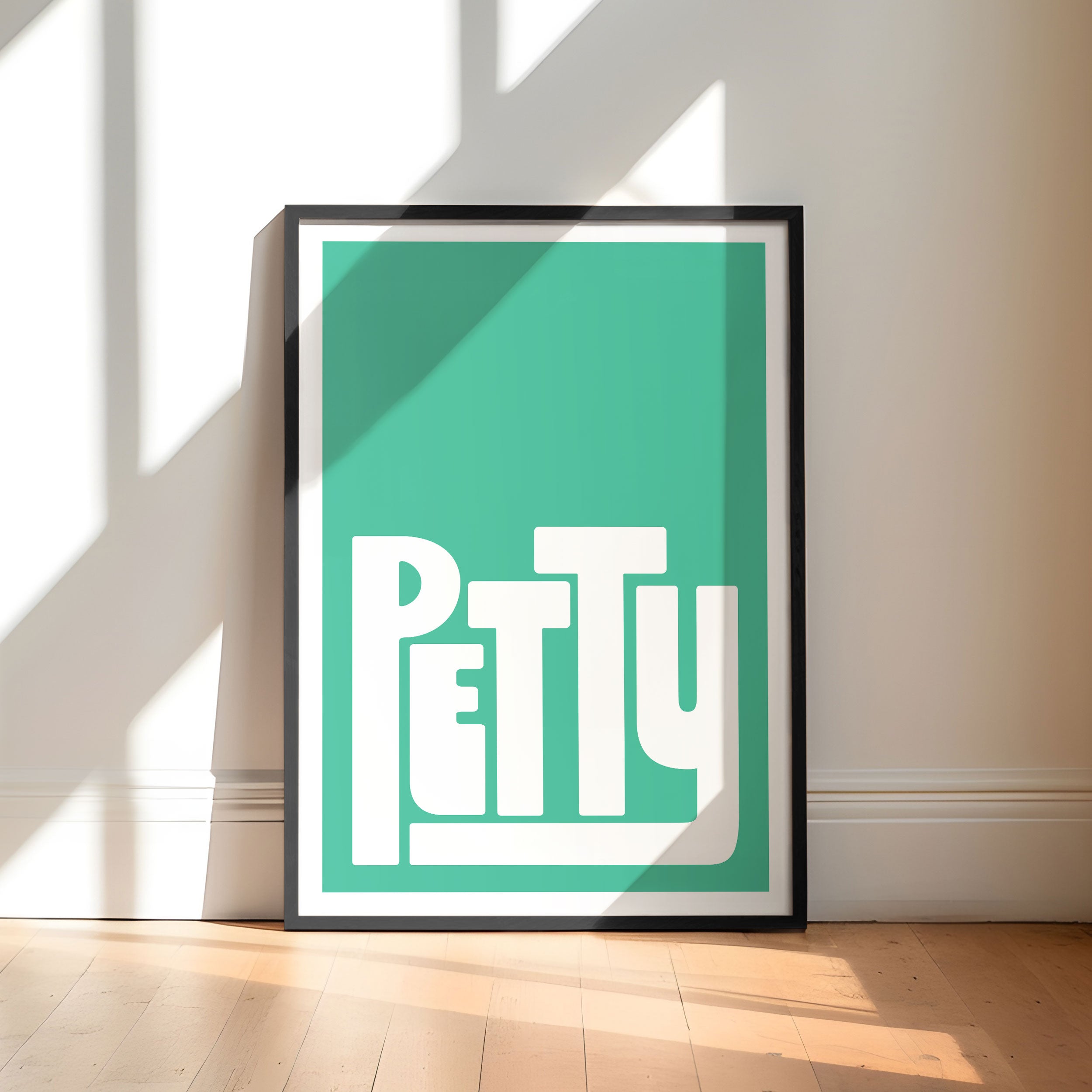 Framed artwork with the word 'Petty' on a teal background, leaning against a wall.