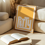 Framed picture with 'PETTY' text on a coffee table in a living room.
