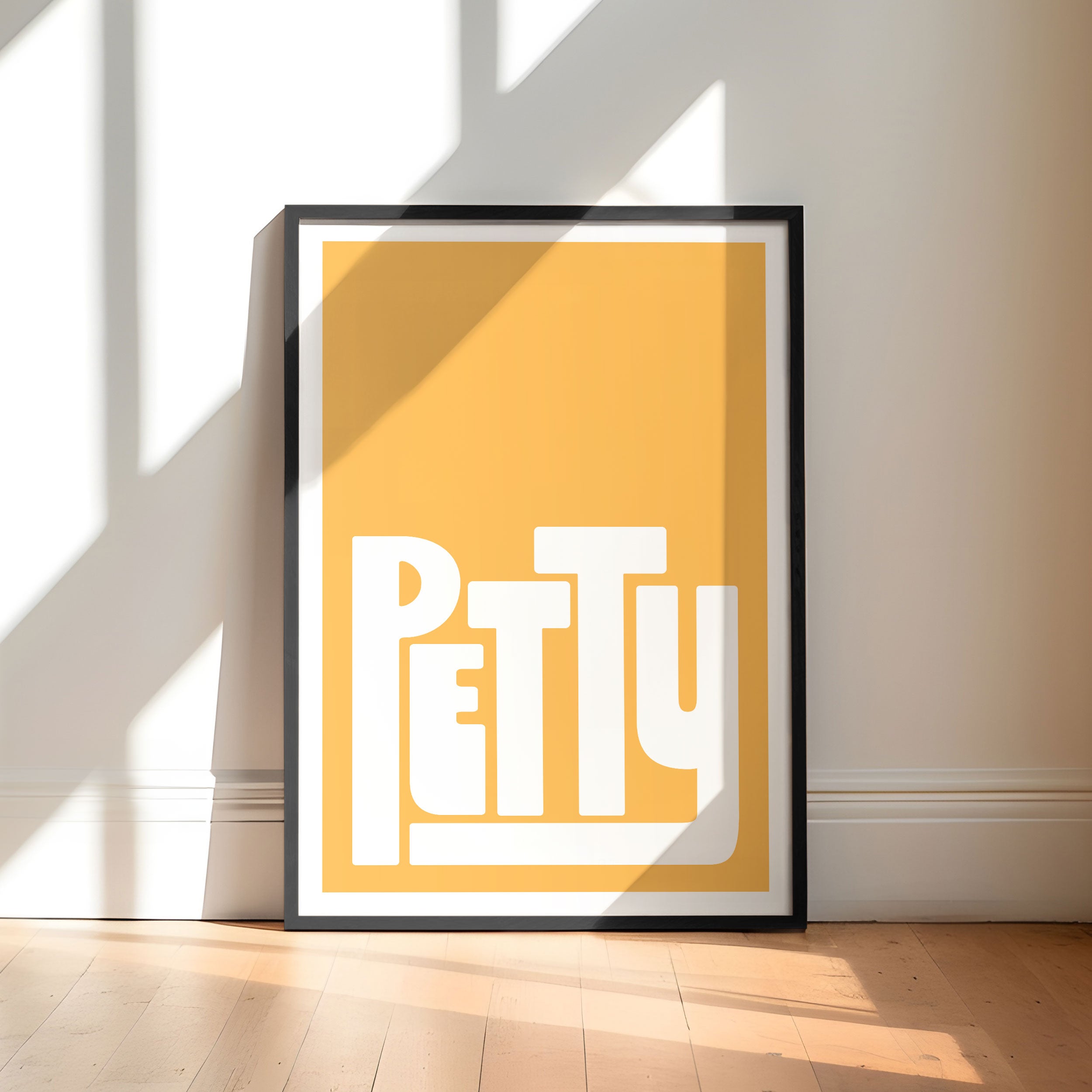 Framed artwork with 'PETTY' text on a yellow background in a minimalistic room.