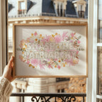 Framed artwork with 'SMASH THE PATRIARCHY' text and floral design held in front of a building.