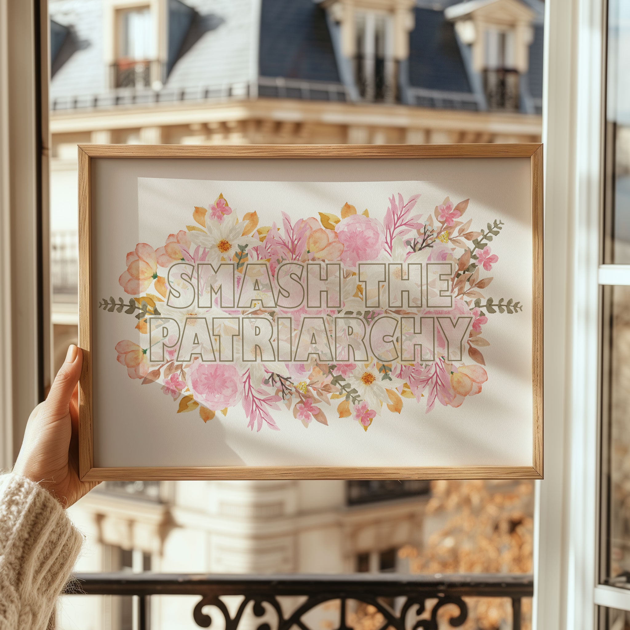 Framed artwork with 'SMASH THE PATRIARCHY' text and floral design held in front of a building.