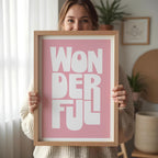 Person holding a framed poster with 'WONDERFUL' text on a pink background