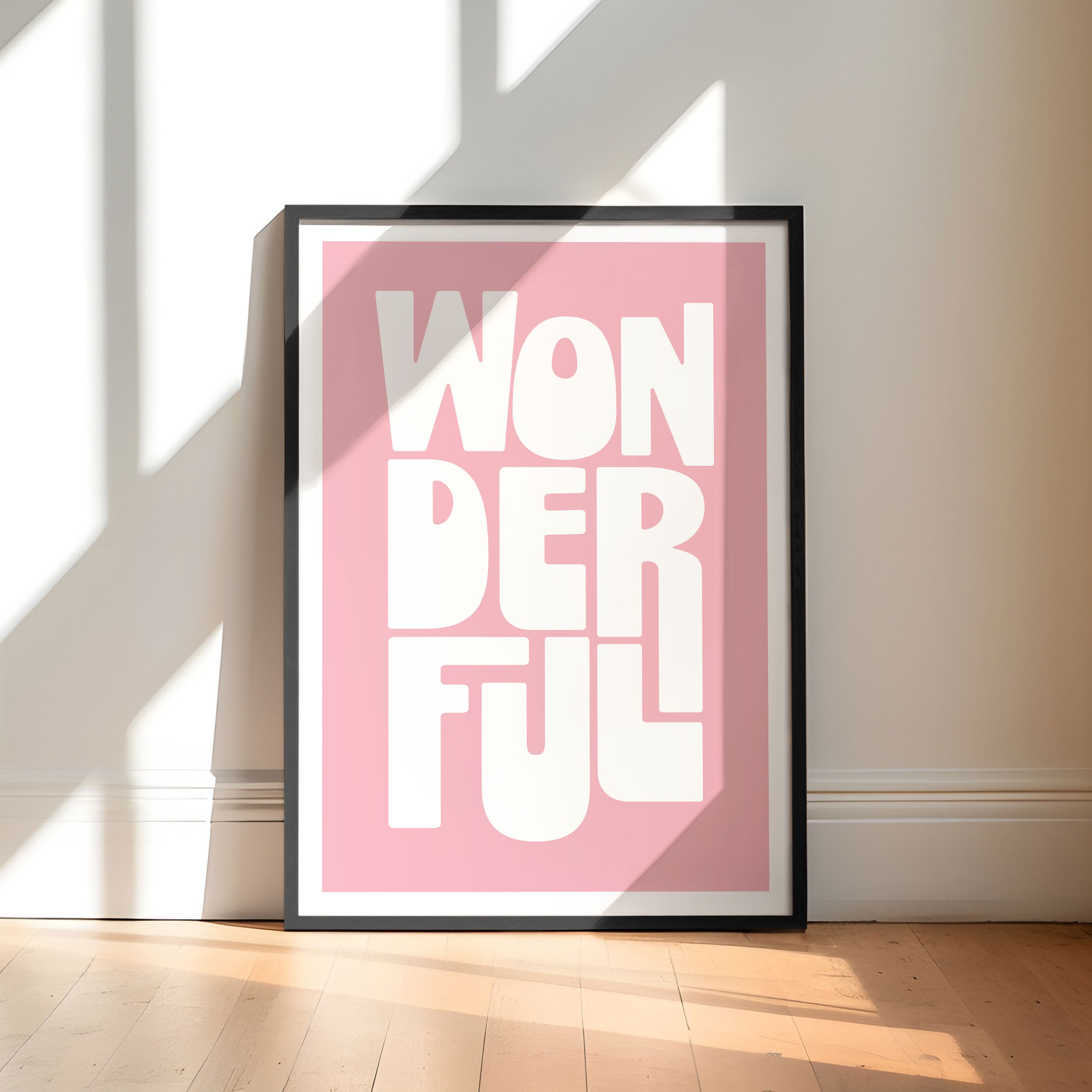 Framed poster with 'WONDERFUL' text on a pink background, placed against a white wall.
