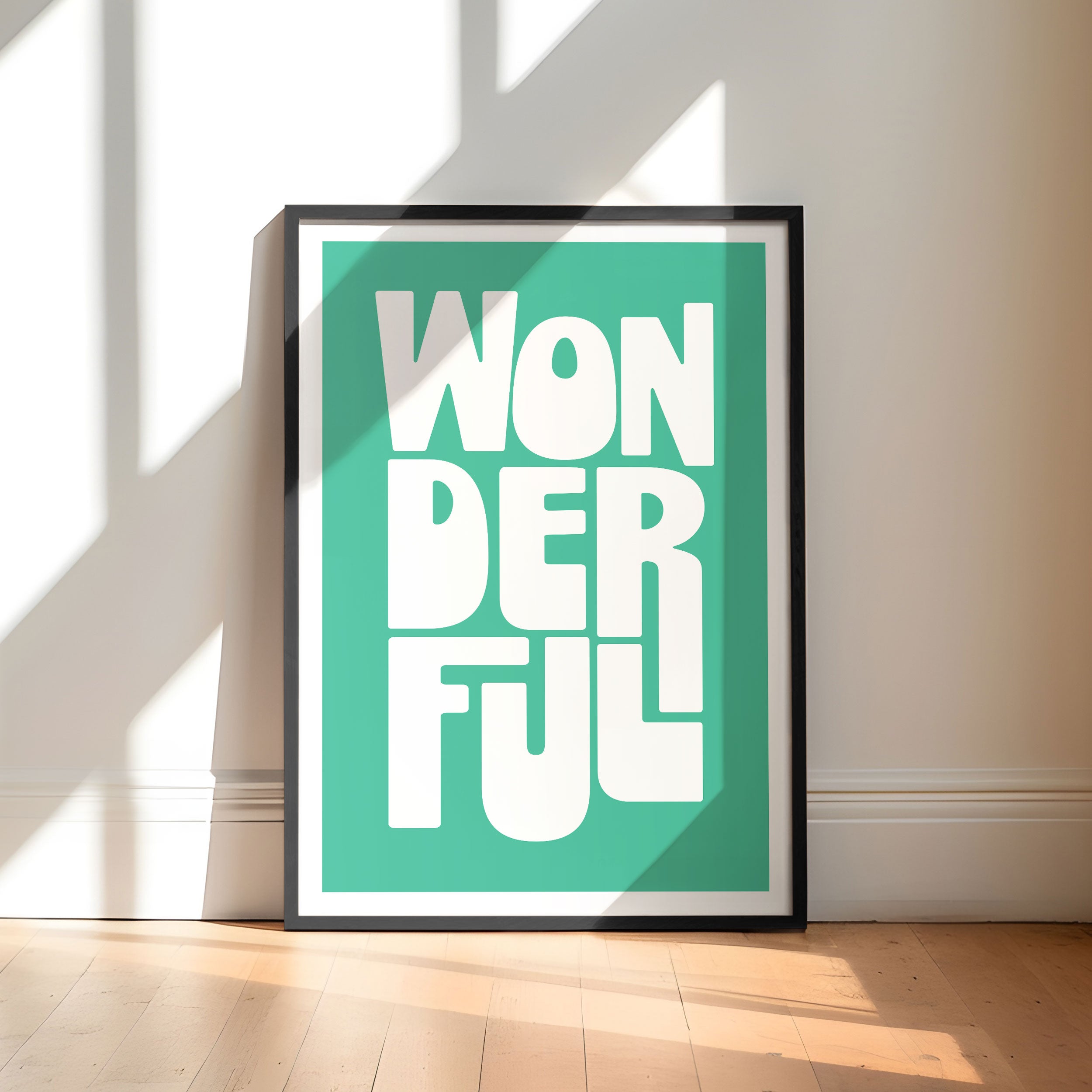 Framed poster with 'WONDERFUL' text on a teal background, placed on a wooden floor with sunlight casting shadows.